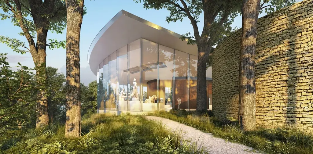 Vista cercana del pabellón principal del Centro Cultural Lola Mora, con amplios ventanales de vidrio que permiten ver esculturas en su interior. El edificio se integra con la naturaleza, rodeado de árboles y muros de piedra. Un sendero de tierra conduce a la entrada del pabellón.